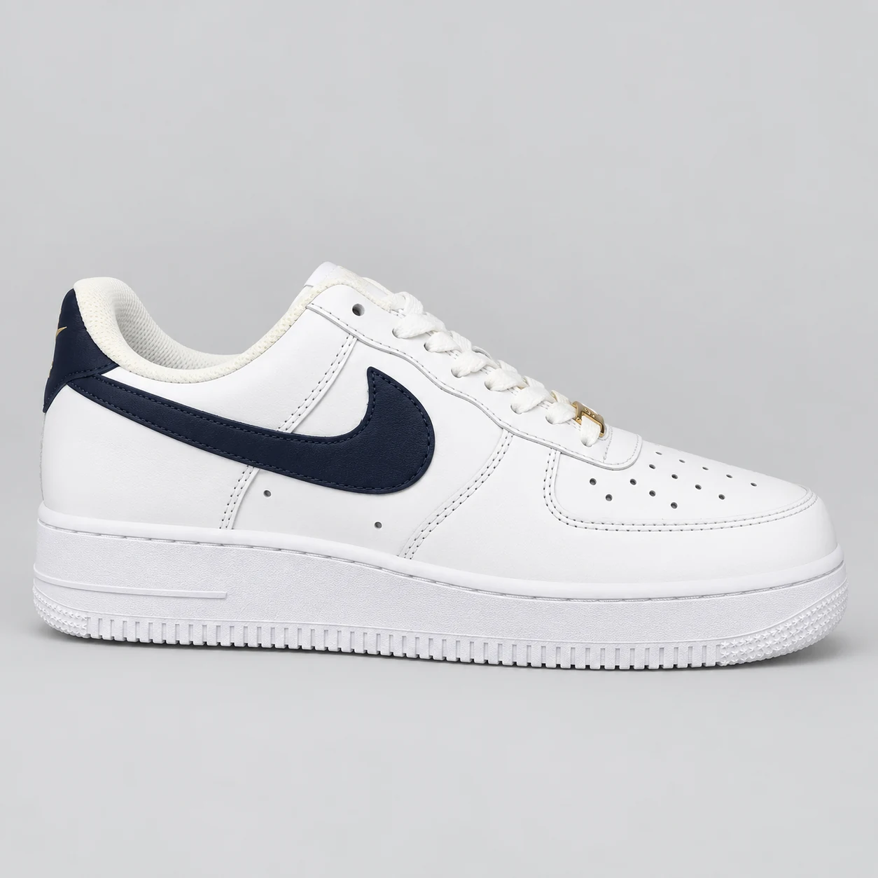 Nike Air Force 1 — White / Navy / Gold A white low-top sneaker with navy Swoosh and heel panels, small gold accents, a perforated toe and a white sole. Choose a UK size from 3 to 9 and view the product photos at The Drip Society.