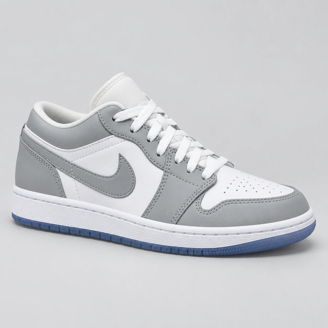 Air Jordan 1 Low — Grey / White / Blue A grey and white low-top sneaker with matching grey Swoosh panels, white laces, a perforated toe and a blue outsole. Choose a UK size from 3 to 9 and view the product photos at The Drip Society.