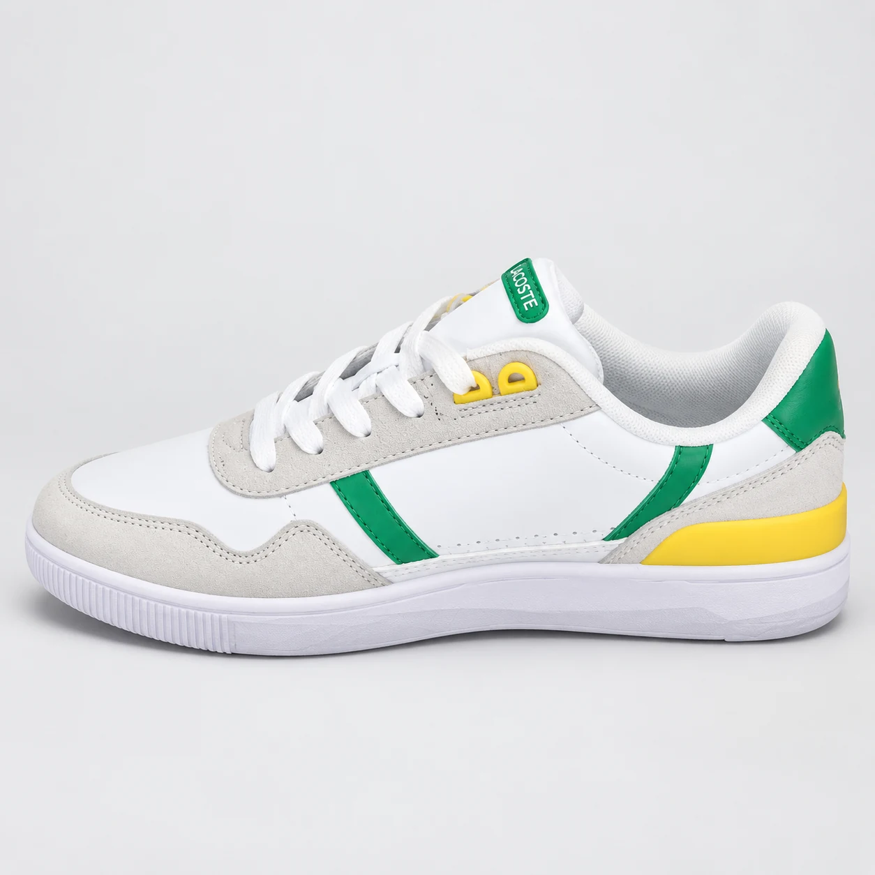 Lacoste T-Clip — White / Grey / Green / Yellow A white and grey low-top sneaker with green side stripes, yellow eyelet and sole accents, and white laces. Choose a UK size from 3 to 9 and view the product photos at The Drip Society.